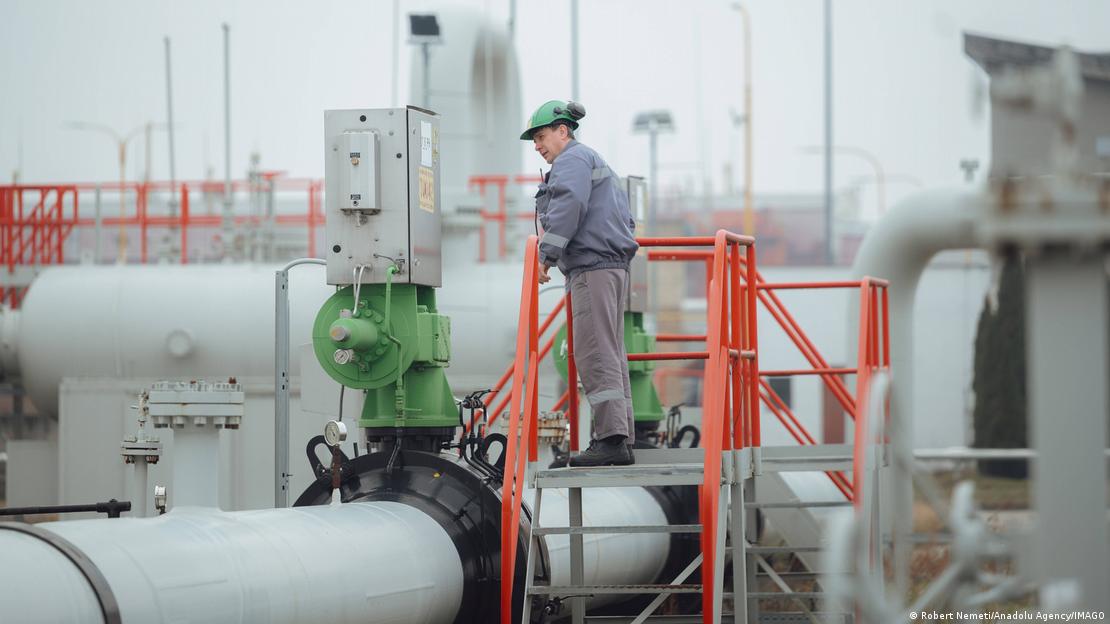Bir doğal gaz dağıtım tesisindeki beyaz boru üzerinde duran, başında kask taşıyan bir görevli